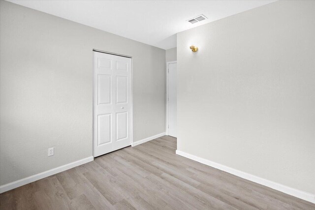 unfurnished bedroom featuring visible vents, baseboards, a closet, and wood finished floors