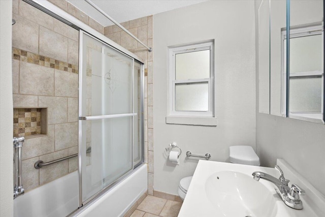 full bath with baseboards, toilet, shower / bath combination with glass door, tile patterned floors, and a sink