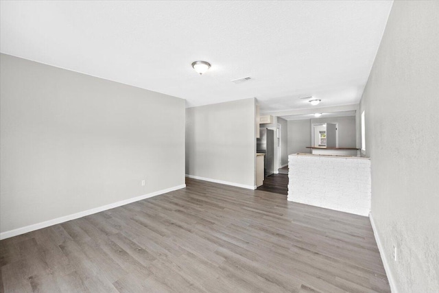 unfurnished living room featuring visible vents, baseboards, and dark wood-type flooring