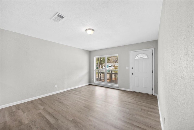 interior space with a textured ceiling, wood finished floors, visible vents, and baseboards