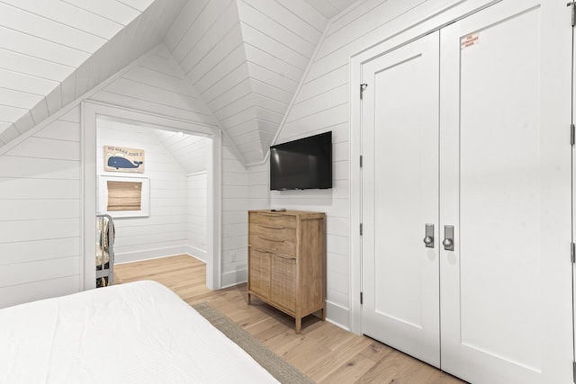 bedroom with lofted ceiling, light wood-type flooring, and wood walls