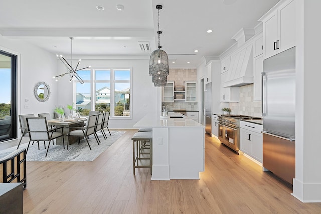 kitchen featuring a kitchen bar, high quality appliances, a sink, light wood-style floors, and custom exhaust hood