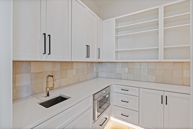 kitchen featuring open shelves, a sink, light countertops, white cabinets, and backsplash