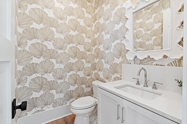 bathroom with toilet, wood finished floors, vanity, and wallpapered walls