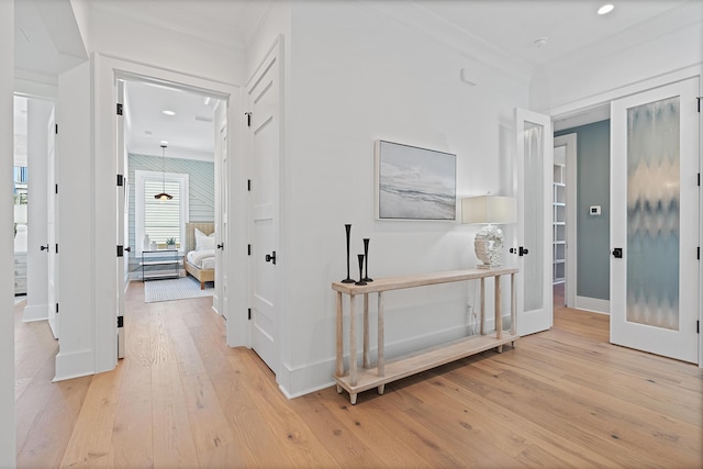 corridor with light wood finished floors, crown molding, and baseboards