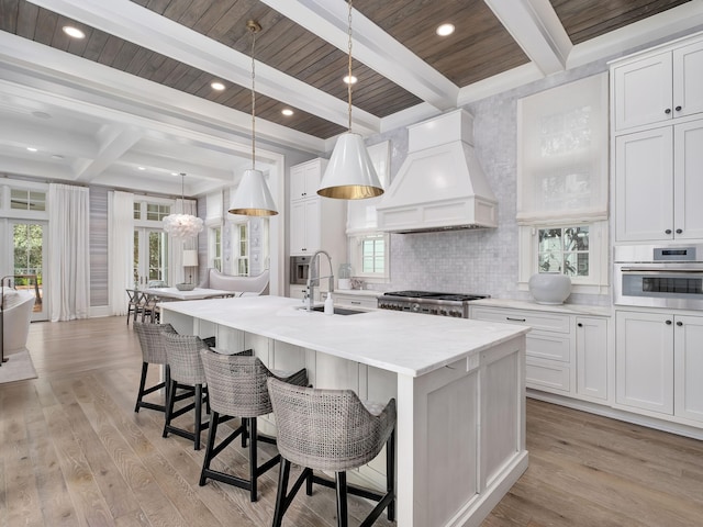 kitchen with oven, light wood-type flooring, a kitchen island with sink, custom range hood, and stove