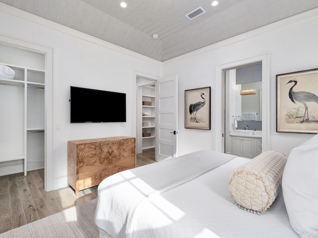 bedroom featuring visible vents, a walk in closet, wood finished floors, a closet, and crown molding