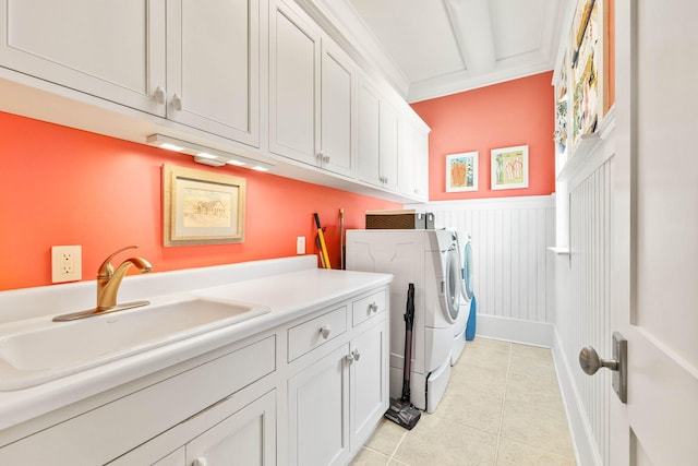 washroom with a sink, cabinet space, wainscoting, light tile patterned floors, and washing machine and clothes dryer