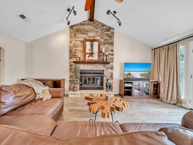 living room with wood finished floors, visible vents, a ceiling fan, lofted ceiling with beams, and a stone fireplace