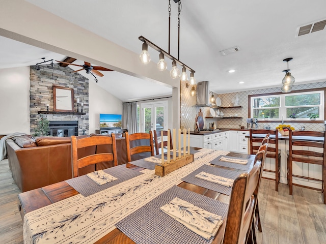 dining room featuring visible vents, vaulted ceiling with beams, a fireplace, ceiling fan, and light wood-style floors