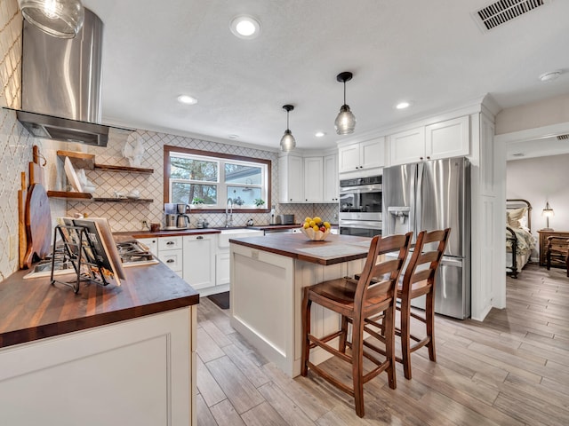 kitchen with visible vents, wooden counters, appliances with stainless steel finishes, wall chimney exhaust hood, and tasteful backsplash