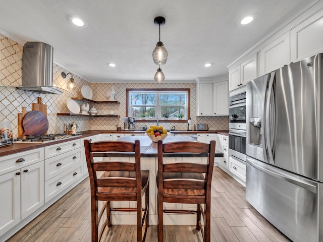 kitchen with wall chimney exhaust hood, light wood-type flooring, wooden counters, and stainless steel appliances