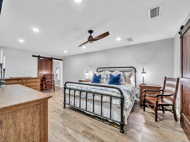 bedroom with visible vents, recessed lighting, light wood-type flooring, and a barn door