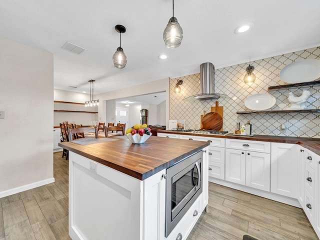 kitchen featuring visible vents, butcher block countertops, stainless steel appliances, and wall chimney range hood