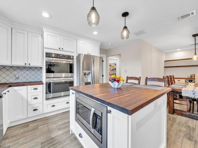 kitchen with tasteful backsplash, butcher block countertops, stainless steel appliances, and visible vents