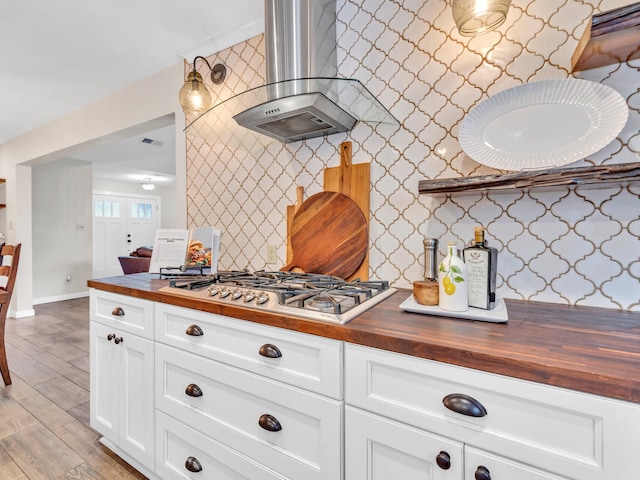 kitchen featuring baseboards, light wood finished floors, wooden counters, stainless steel gas stovetop, and wall chimney range hood