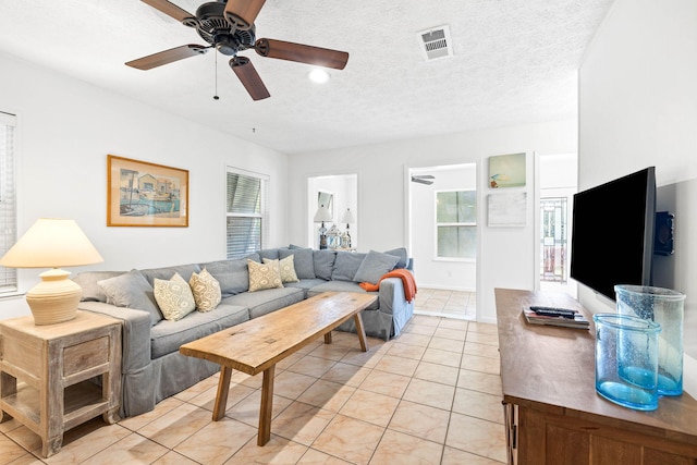 living area featuring ceiling fan, light tile patterned floors, visible vents, and a textured ceiling