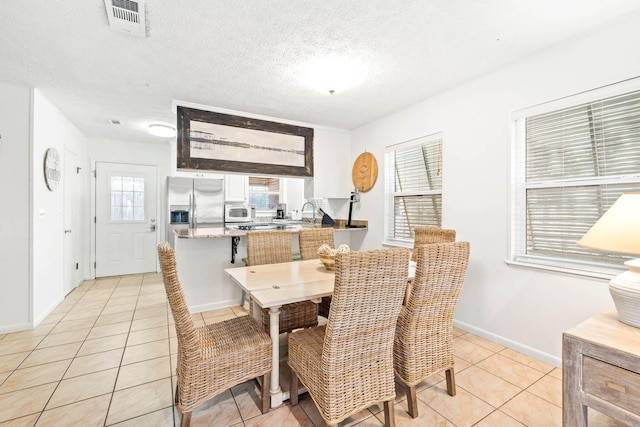 dining room with light tile patterned floors, visible vents, baseboards, and a textured ceiling