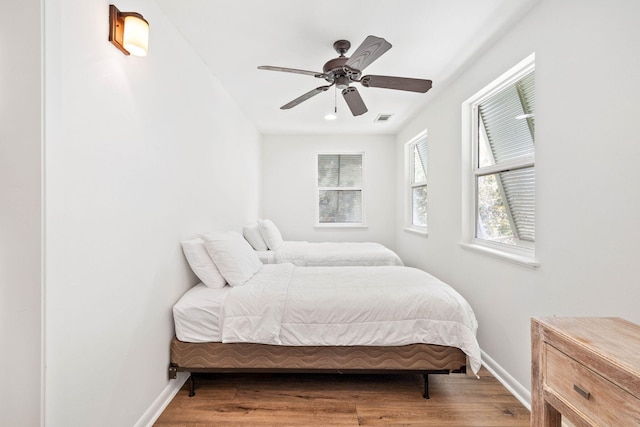 bedroom with visible vents, baseboards, wood finished floors, and a ceiling fan