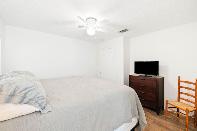 bedroom with visible vents, a textured ceiling, ceiling fan, and wood finished floors