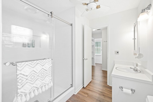 bathroom with a ceiling fan, wood finished floors, a shower stall, baseboards, and vanity