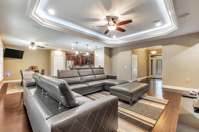 living room with a ceiling fan, baseboards, visible vents, a tray ceiling, and dark wood-type flooring