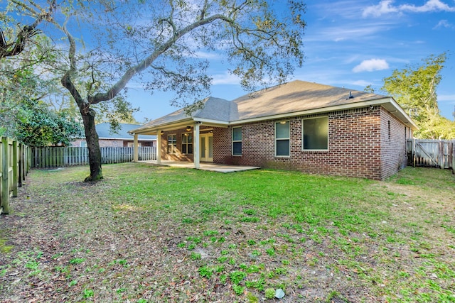 rear view of house with a ceiling fan, a fenced backyard, a lawn, a patio area, and brick siding