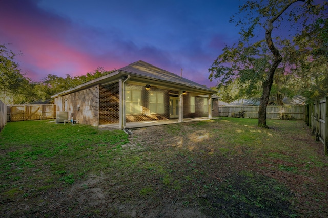 back of house at dusk with a patio area, a yard, a fenced backyard, and brick siding