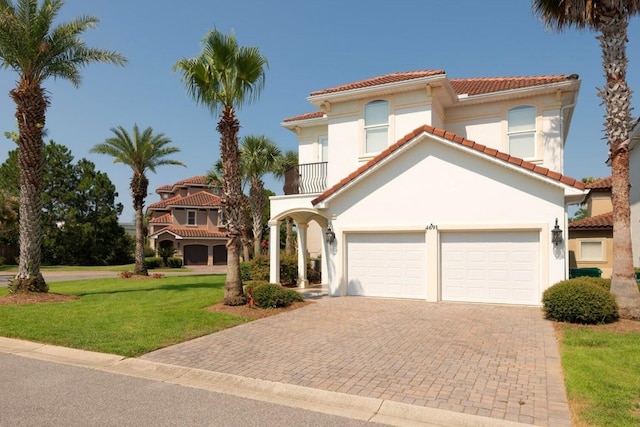 mediterranean / spanish-style home with a front yard, a balcony, stucco siding, a garage, and decorative driveway