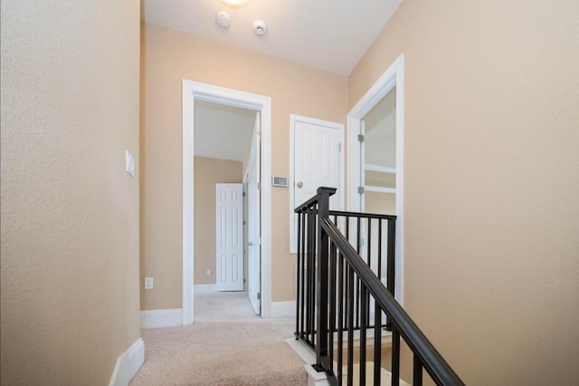 corridor with an upstairs landing, light colored carpet, and baseboards