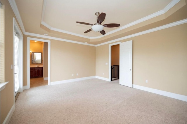 unfurnished bedroom featuring crown molding, baseboards, light carpet, ensuite bathroom, and a raised ceiling