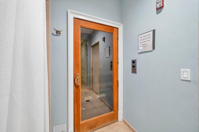 hall featuring light tile patterned flooring, visible vents, and baseboards