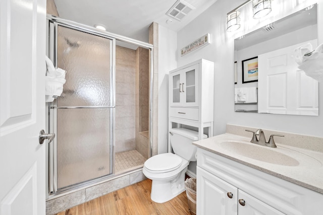 bathroom with visible vents, toilet, wood finished floors, a shower stall, and vanity