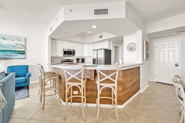 kitchen featuring visible vents, white cabinetry, stainless steel appliances, a peninsula, and light tile patterned floors