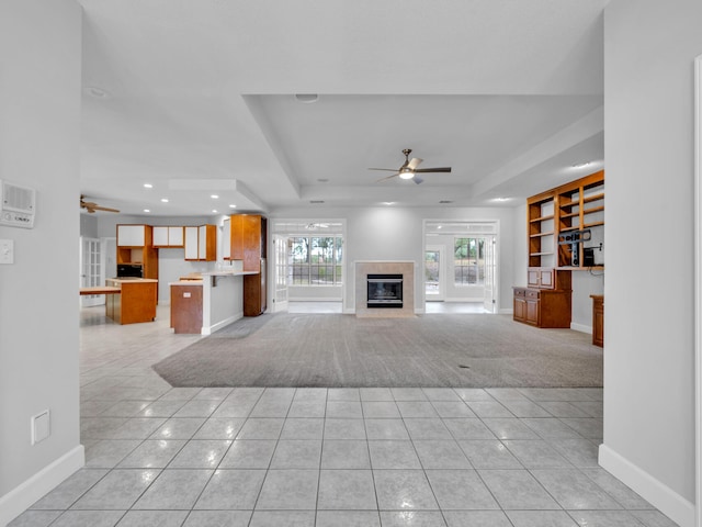 unfurnished living room with light tile patterned floors, a raised ceiling, and a ceiling fan