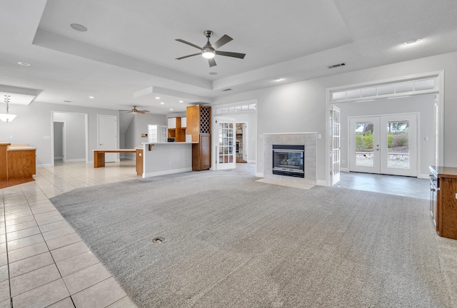 unfurnished living room featuring french doors, a fireplace, a raised ceiling, and ceiling fan