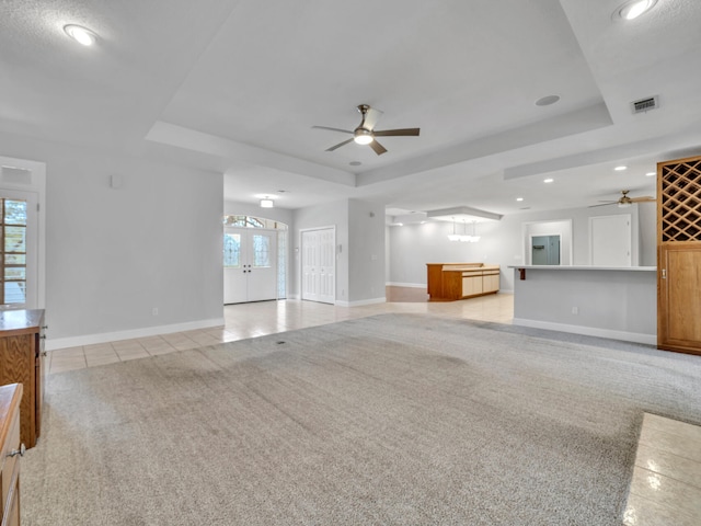 unfurnished living room with visible vents, light carpet, a tray ceiling, light tile patterned flooring, and baseboards