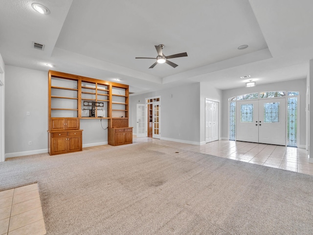 unfurnished living room featuring a tray ceiling, light carpet, visible vents, and french doors