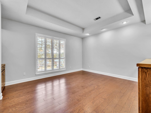 interior space featuring a tray ceiling, baseboards, visible vents, and wood finished floors