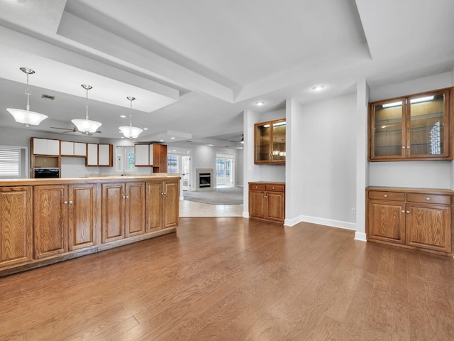 kitchen with glass insert cabinets, baseboards, a tray ceiling, brown cabinets, and wood finished floors