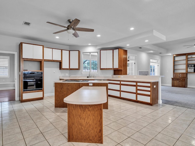 kitchen featuring visible vents, black oven, a kitchen island, a peninsula, and ceiling fan