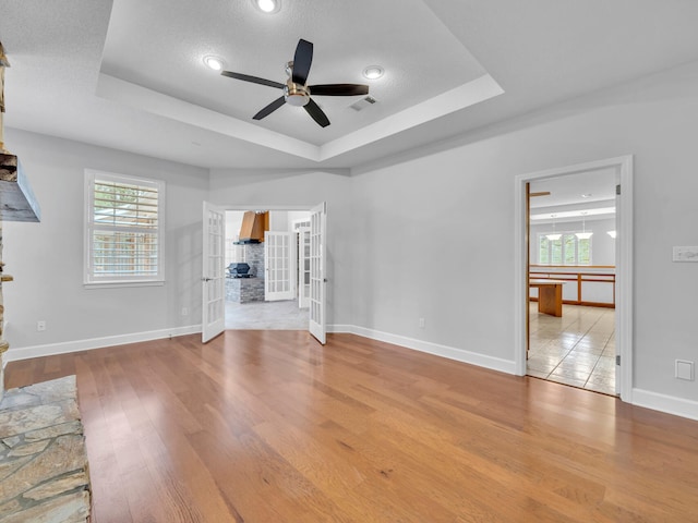 unfurnished living room featuring a tray ceiling, wood finished floors, a healthy amount of sunlight, and visible vents