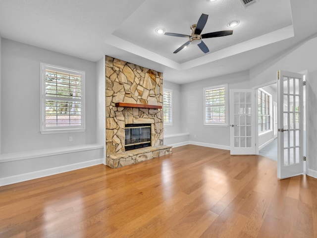 unfurnished living room with a tray ceiling, a healthy amount of sunlight, wood finished floors, and a fireplace