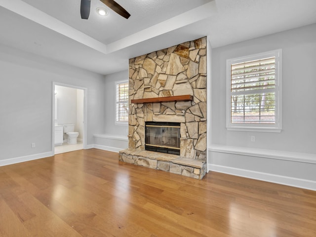 unfurnished living room featuring a fireplace, a raised ceiling, baseboards, and wood finished floors