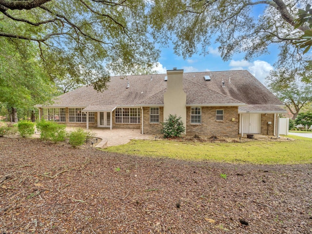 rear view of property with brick siding, roof with shingles, a chimney, a yard, and a patio area