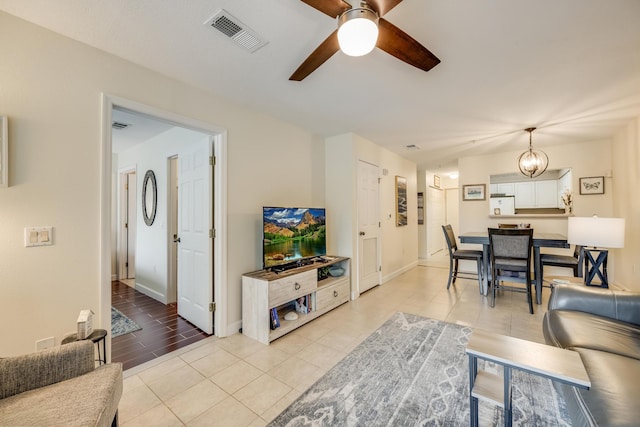 living room with light tile patterned floors, visible vents, ceiling fan with notable chandelier, and baseboards