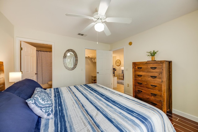 bedroom featuring a spacious closet, visible vents, baseboards, wood finished floors, and a ceiling fan