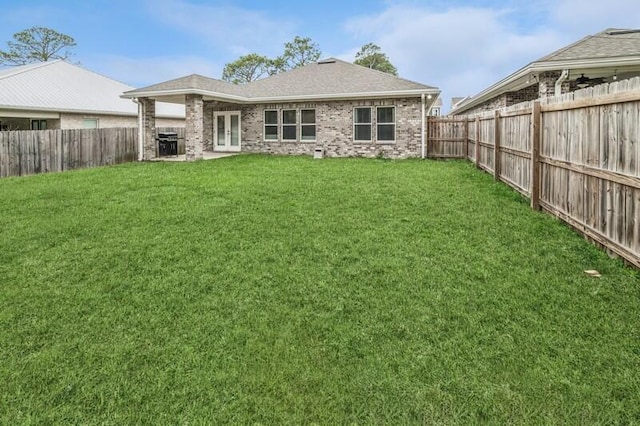 back of house with brick siding, roof with shingles, french doors, a fenced backyard, and a yard