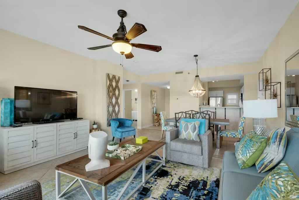 living room with light tile patterned flooring and ceiling fan with notable chandelier