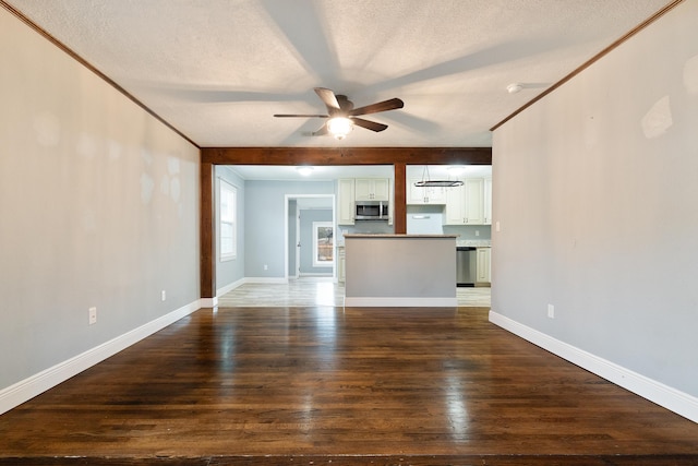 unfurnished living room with wood finished floors, baseboards, ornamental molding, ceiling fan, and a textured ceiling